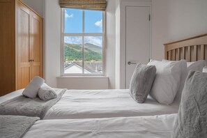 A bedroom with a bed, a wardrobe, a window with a view of hills and buildings, and a door.