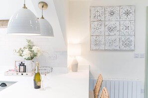A modern kitchen with white cabinetry, a pendant light, a decorative wall tile, and a wicker chair. - Otterbield, Apartment 4, ,Derwent House (Portinscale)