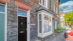 Un bâtiment à la façade en pierre, avec une porte noire, une fenêtre à cadre blanc et un panneau de signalisation.