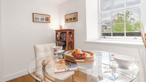Un coin repas avec une table en verre, un buffet en bois, des tableaux encadrés au mur et une fenêtre donnant sur un beau paysage.