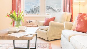 Una sala de estar acogedora con un sofá, sillones, una mesa de centro y vistas a montañas a través de una ventana.
