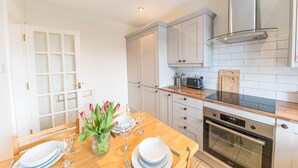 Una cocina moderna con armarios blancos, una mesa de comedor de madera servida con platos, vasos y un jarrón de flores.