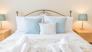 Una cama bien hecha con una colcha estampada de flores, dos lámparas de noche y un cabecero de madera.