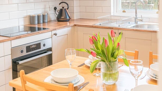 Una cocina moderna con armarios blancos, una campana extractora de acero inoxidable, una tetera y un comedor con una mesa lista para dos personas.