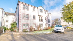 A two-story residential building with a white facade and pink trim, a driveway, and a parked car. - 16 Greta Grove House (Keswick)