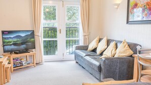 A living room with a grey sofa, a television, a wooden coffee table, and a bookshelf. - 16 Greta Grove House (Keswick)