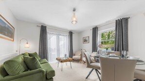 Een moderne woonkamer met een groene bank, een eettafel met stoelen, en een raam met gordijnen.