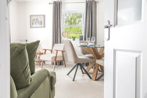 Ein Zimmer mit einem grünen Sofa, einem Esstisch mit Stühlen, einem Fenster mit Vorhängen und einer Tür.