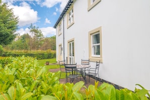 Ein weißes Gebäude mit einer Terrasse, die einen Tisch und Stühle bietet, umgeben von viel Grün.