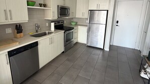 Una cocina moderna con armarios blancos, electrodomésticos de acero inoxidable y piso de baldosas.
