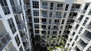 Un edificio residencial alto con varios balcones, un patio central con asientos y palmeras.