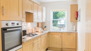 Una cocina moderna con armarios de madera, horno empotrado, estufa a gas y ventana con vista a zonas verdes.