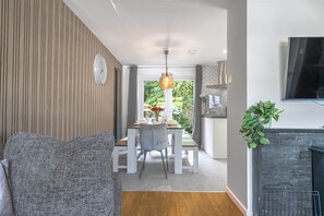 Ein modernes Wohnzimmer mit Kamin, einem Essbereich mit Blick und einer Küche mit Fernseher.