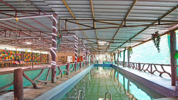 An indoor swimming pool with a wooden deck, metal beams, and a colorful wall. - Deluxe Ranihati Tripureswari (Howrah)