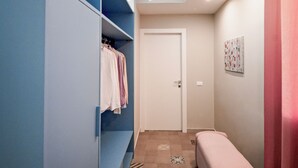 Ein schmaler Flur mit einem blauen Schrank, einer Bank, gefliestem Boden mit Muster und einer Tür am Ende.