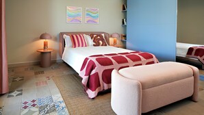 Ein modernes Schlafzimmer mit einem großen Bett, Nachttischlampen, einem kleinen Tisch, einer Bank und zwei Wandbildern.