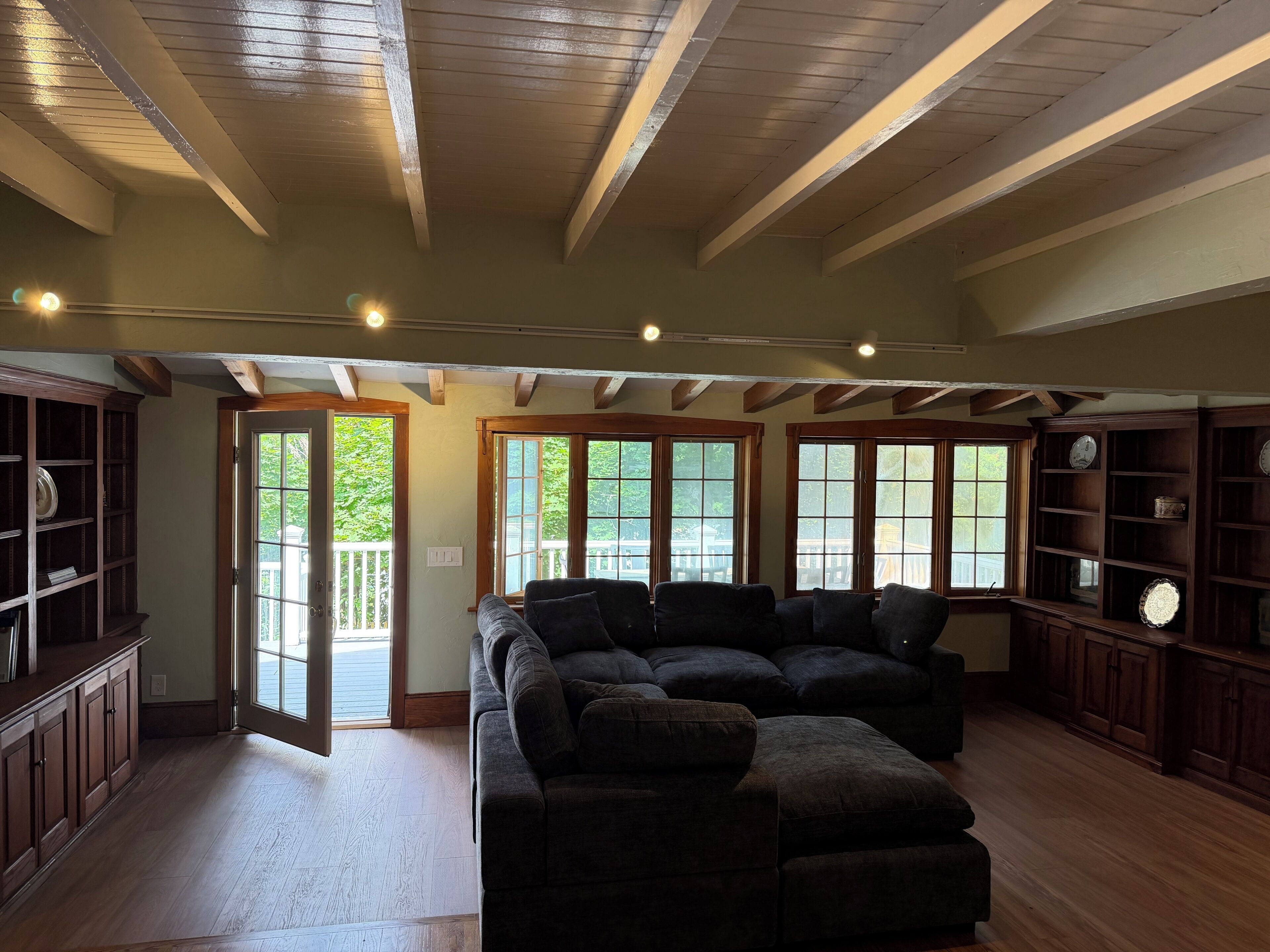 A spacious living room with a sectional sofa, wooden beams on the ceiling, and large windows.