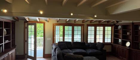 A spacious living room with a sectional sofa, wooden beams on the ceiling, and large windows.