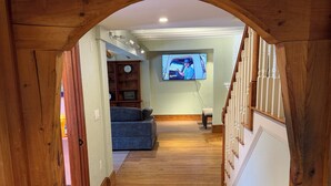 A wooden hallway leading to a living room with a television displaying a man in a truck. - BRAND NEW, Complete renovation: 4-Bedroom, 3.5 Bath, private Annisquam Gem! (Gloucester)