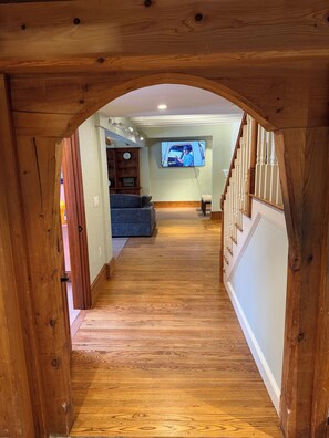 Ein Holzboden führt zu einem Wohnzimmer, in dem ein Fernseher läuft. Zu sehen ist ein Mann in einem Lieferwagen.
