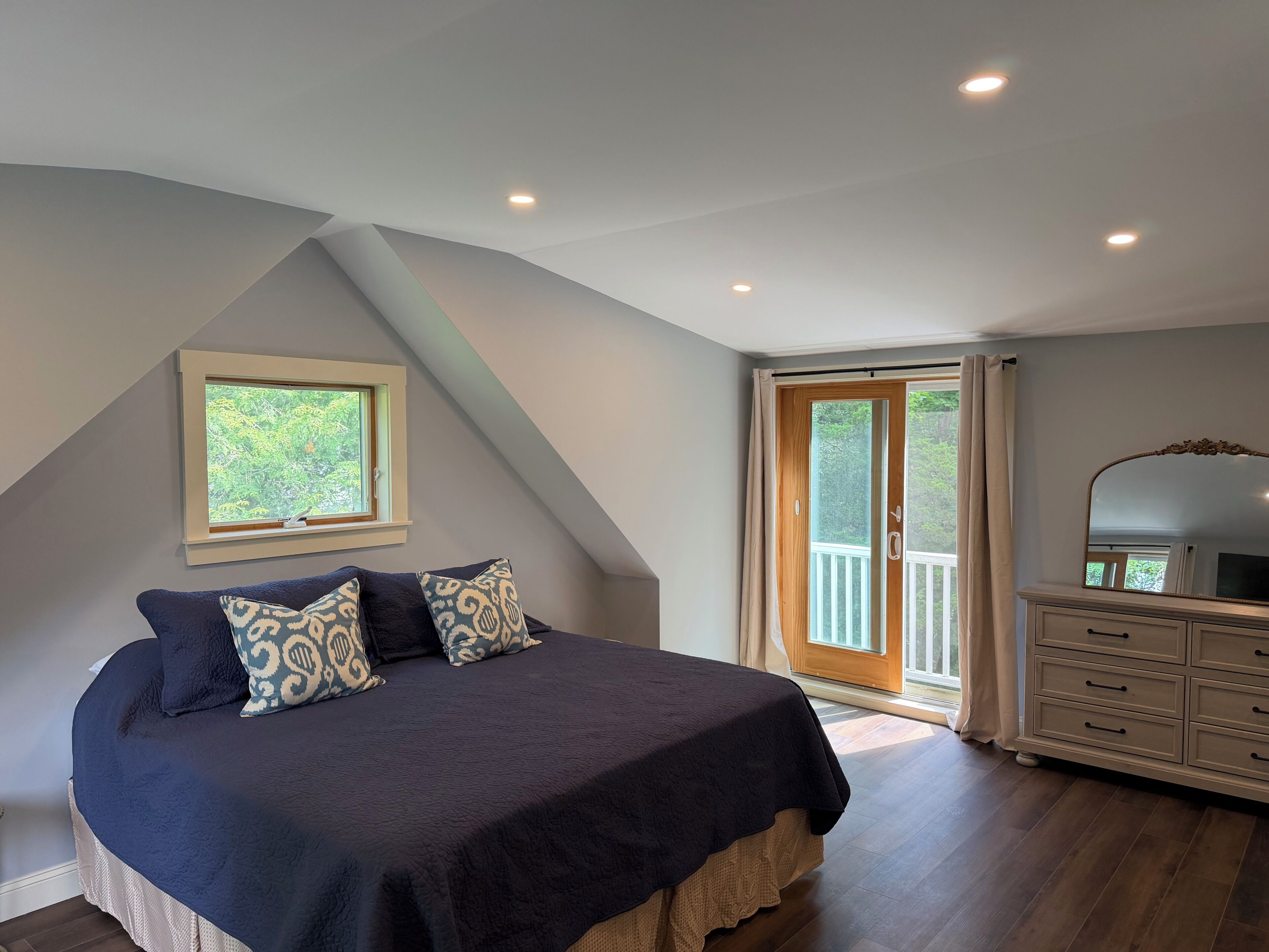 Une chambre à coucher comprenant un lit, une commode, une fenêtre et une porte donnant sur un balcon.