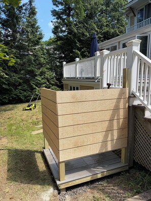 Eine Holzterrasse mit weißer Brüstung, umgeben von einem Garten mit Rasenmäher und Bäumen.