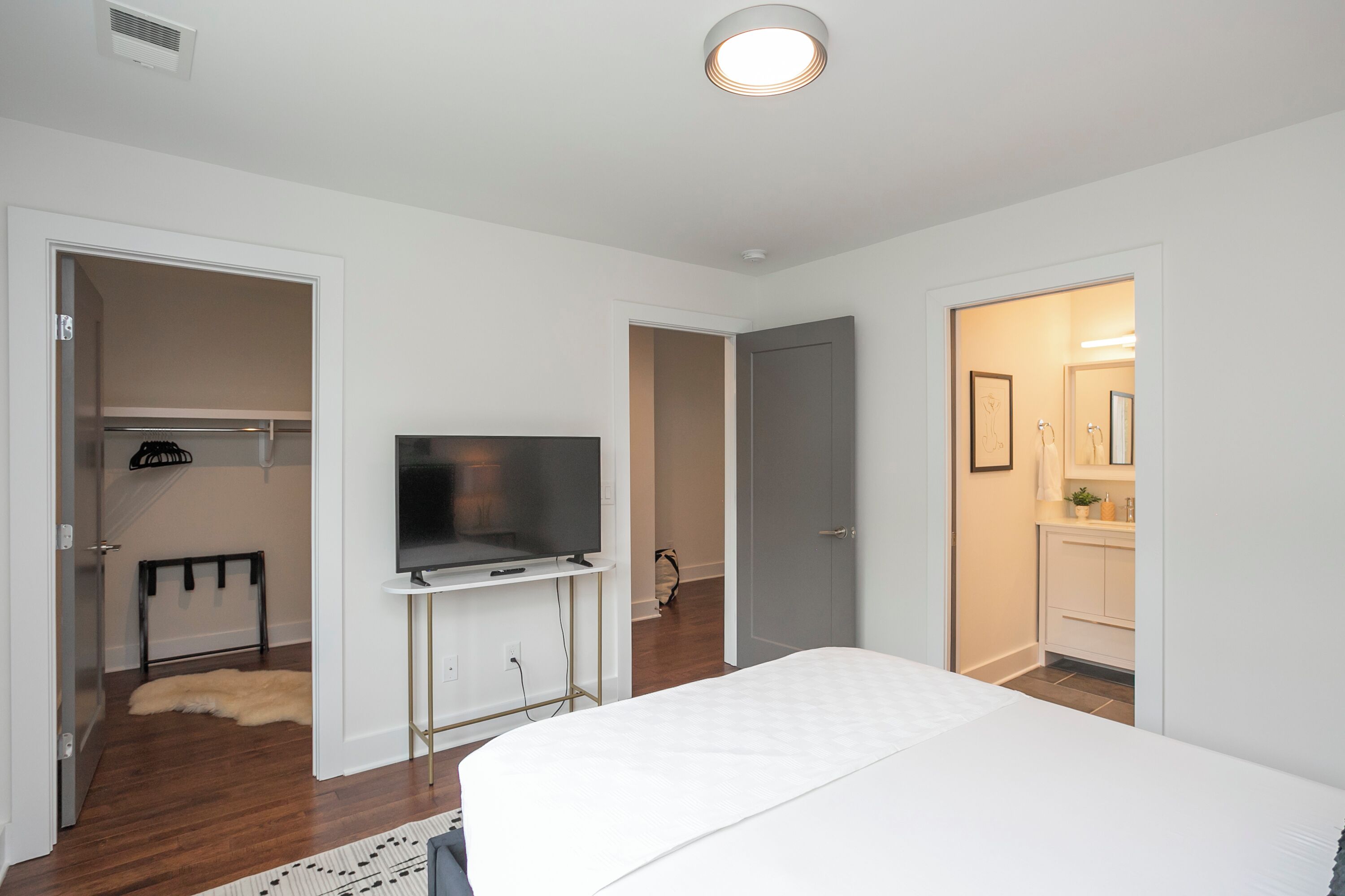 Un dormitorio con cama, televisor sobre un mueble, armario y una puerta que da a un baño.