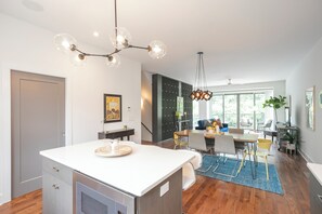 Eine moderne Küche mit Kochinsel, ein Essbereich mit Stühlen und Tisch sowie eine Treppe, die in eine obere Ebene führt.