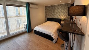 Een hotelkamer met een bed, een bureau met lamp, een raam met gordijnen en een airconditioning.