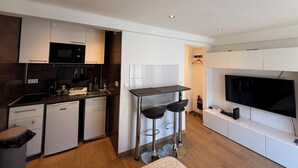 Een moderne keuken met een ingebouwde magnetron, een koffieapparaat en een kleine koelkast. Er staan twee barkrukken en er is een flatscreen televisie aan de muur bevestigd.