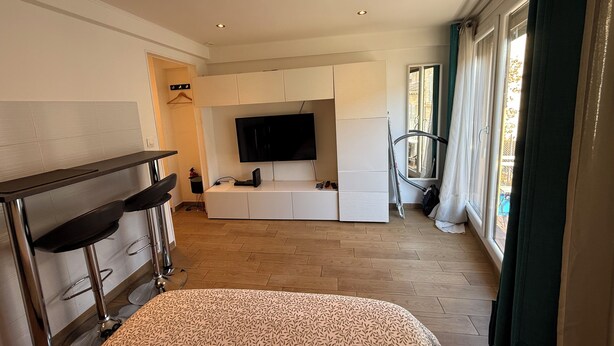 Een moderne woonkamer met een flatscreen televisie, een bank, een salontafel en een eethoek met een barkruk.