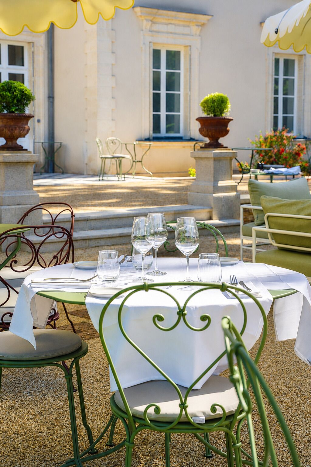 An outdoor dining area with a table set for four, surrounded by green metal chairs.