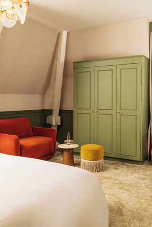 Et hotelværelse med en seng, en rød sofa, en grøn garderobe, en gul fodskammel og et lille rundt bord med en flaske og glas.