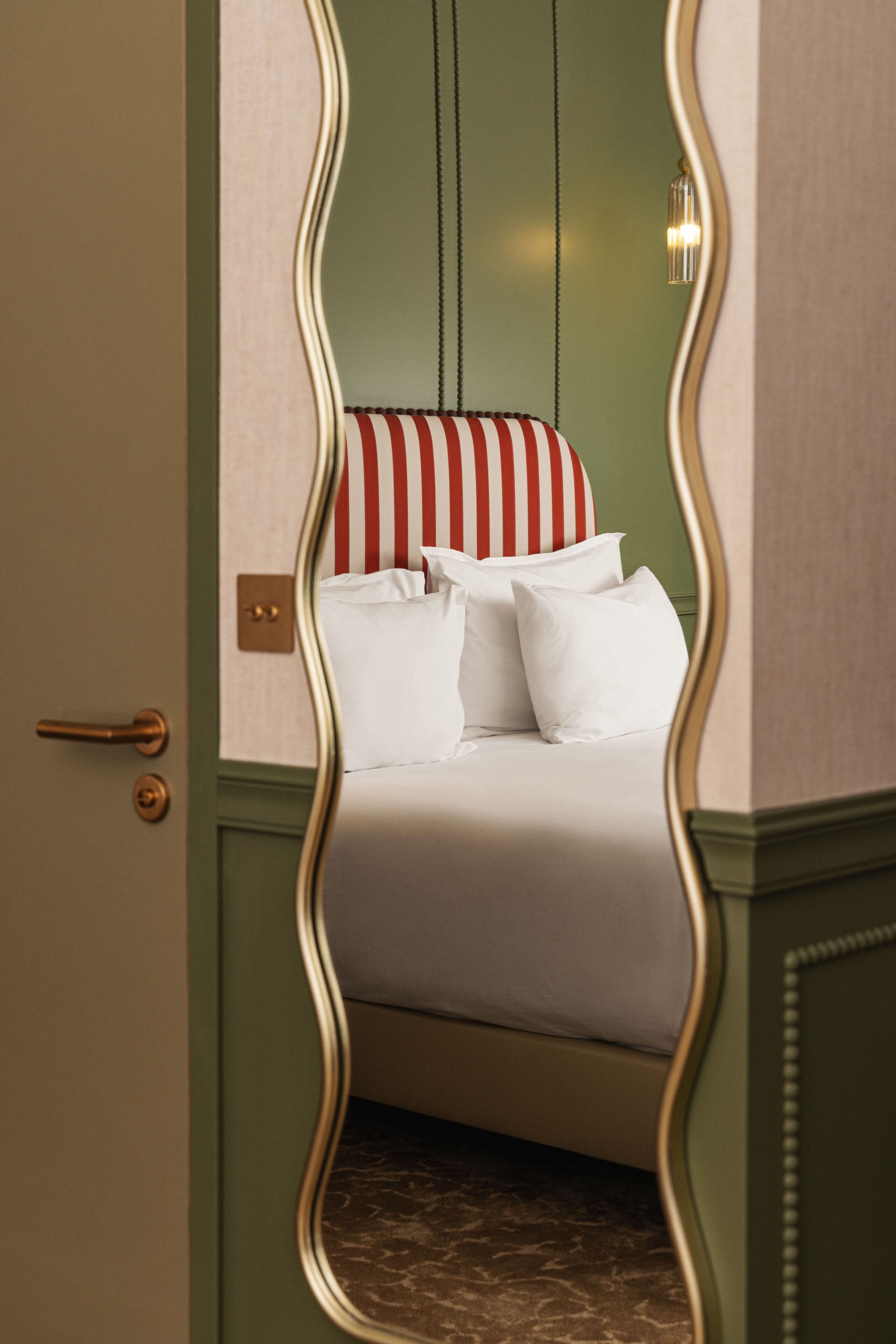 A bed with white bedding and striped pillows, a green wall, and a door with a brass handle.