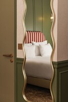 Una cama con ropa blanca y almohadas a rayas, una pared verde y una puerta con picaporte de latón.