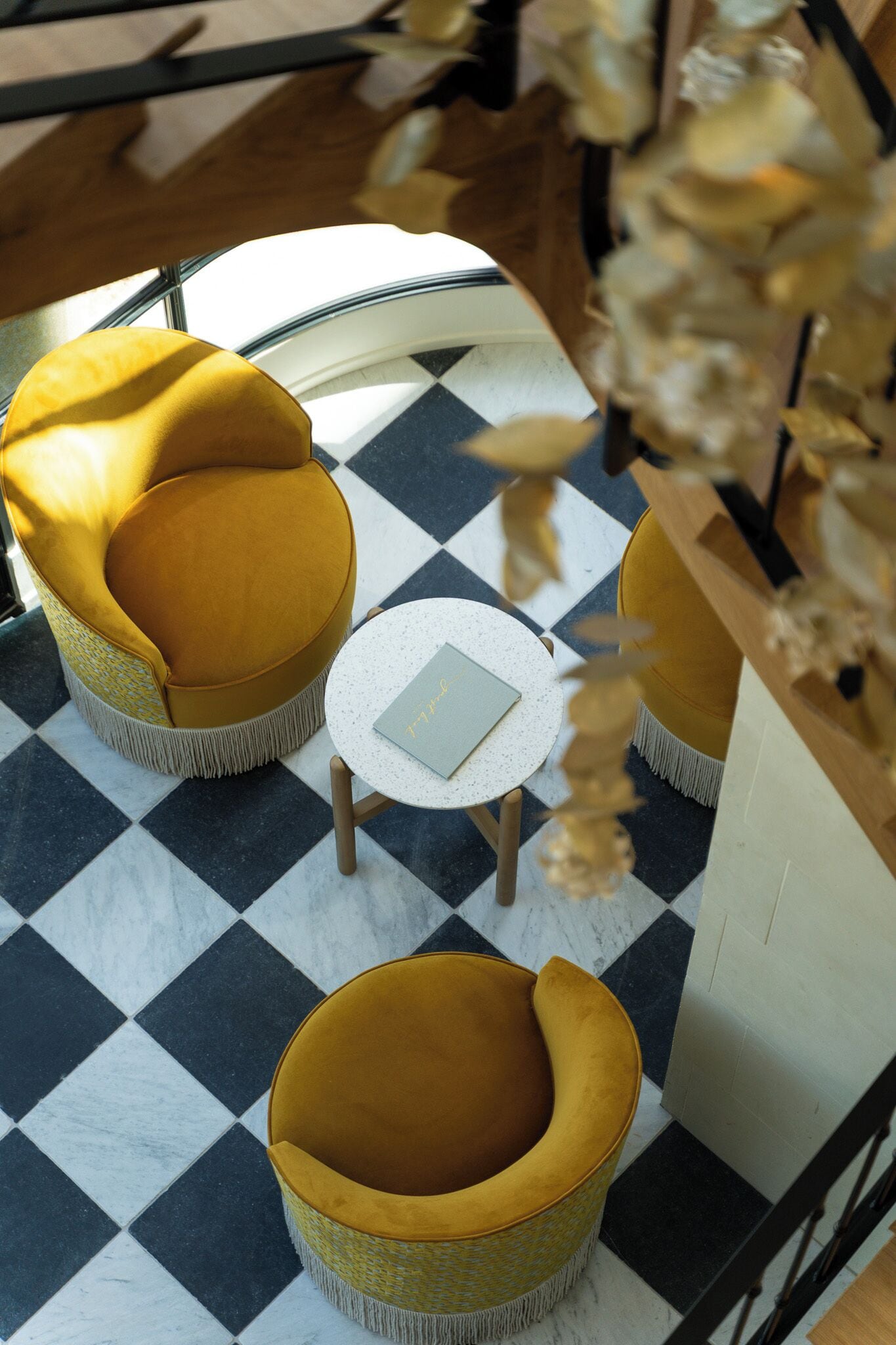 Una habitación con piso a cuadros, dos sillones amarillos, una mesita redonda y un jarrón decorativo.