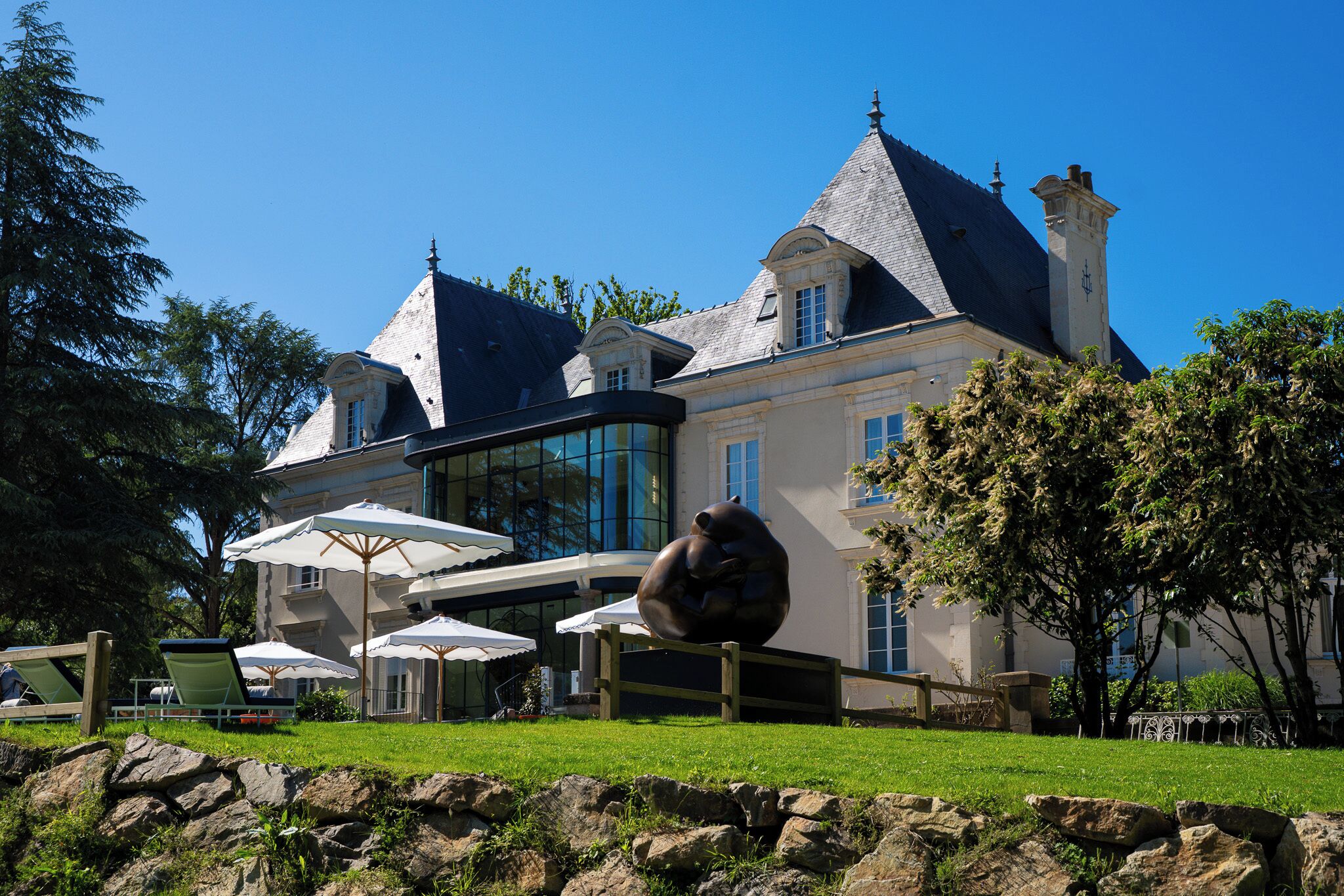 A large stately building with a prominent turret, a conservatory, and outdoor seating with umbrellas.