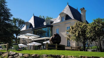 A large stately building with a prominent turret, a conservatory, and outdoor seating with umbrellas.