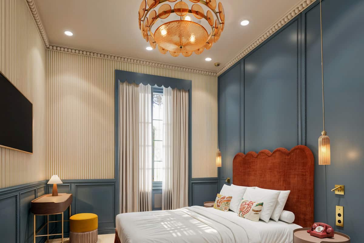 A bedroom with a large bed, a bedside table, a lamp, a telephone, and a wall-mounted light fixture.