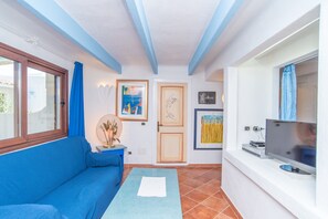 Une pièce avec un canapé bleu, une petite table surmontée d’un miroir, un téléviseur et des œuvres d’art encadrées accrochées au mur.