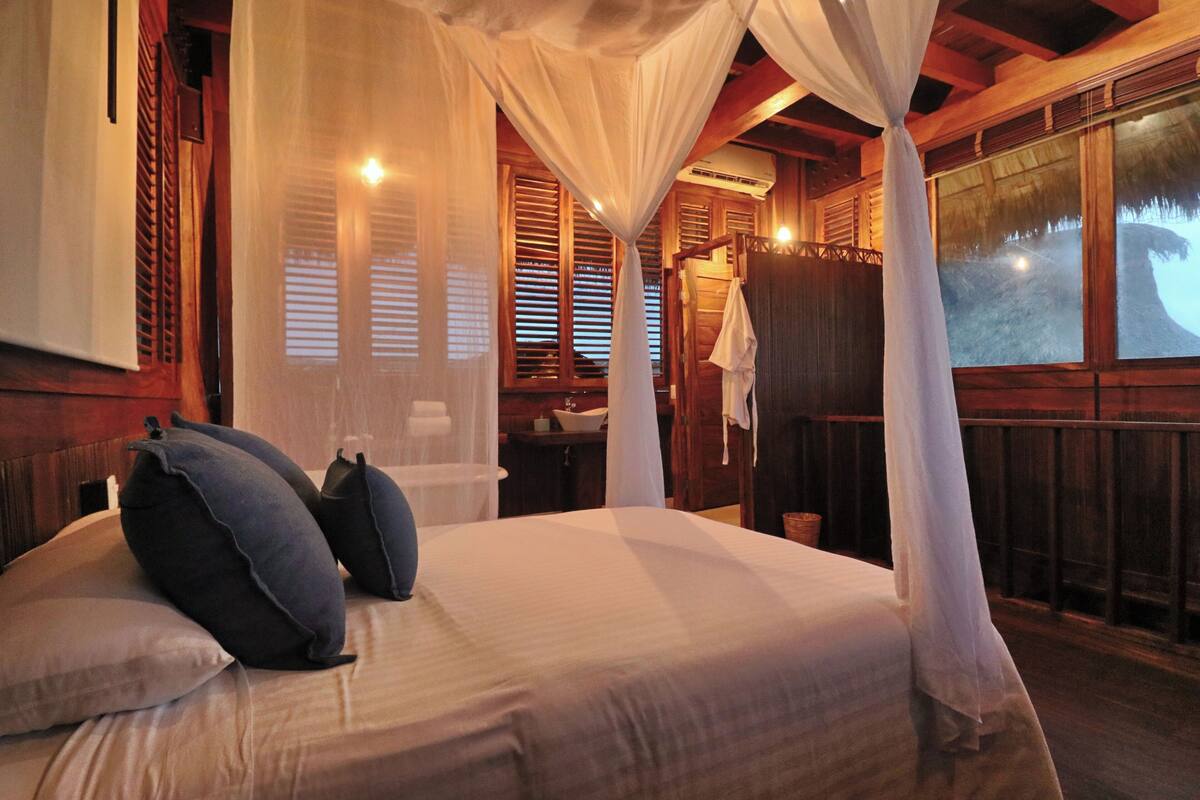 Ein Schlafzimmer mit Bett, Kissen, Baldachin, Holzwänden und einem Fenster.