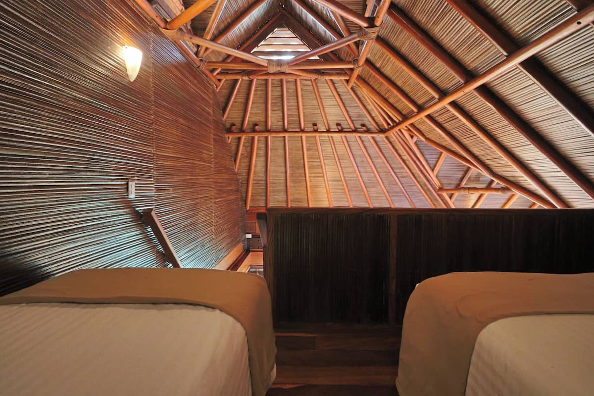 Ein Zimmer mit schrägen Wänden, Holzbalken und zwei Betten.