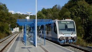Ein Bahnsteig eines Bahnhofs, auf dem ein moderner Zug mit der Aufschrift 'Düren Hbf' einfährt.