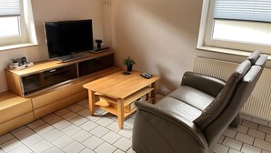 Un espace de vie compact comprenant un téléviseur, des meubles en bois, une petite table, un canapé et un radiateur.