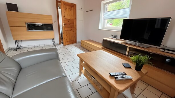 Un salon moderne avec un canapé, une table basse en bois, un téléviseur et une fenêtre donnant sur un paysage verdoyant.