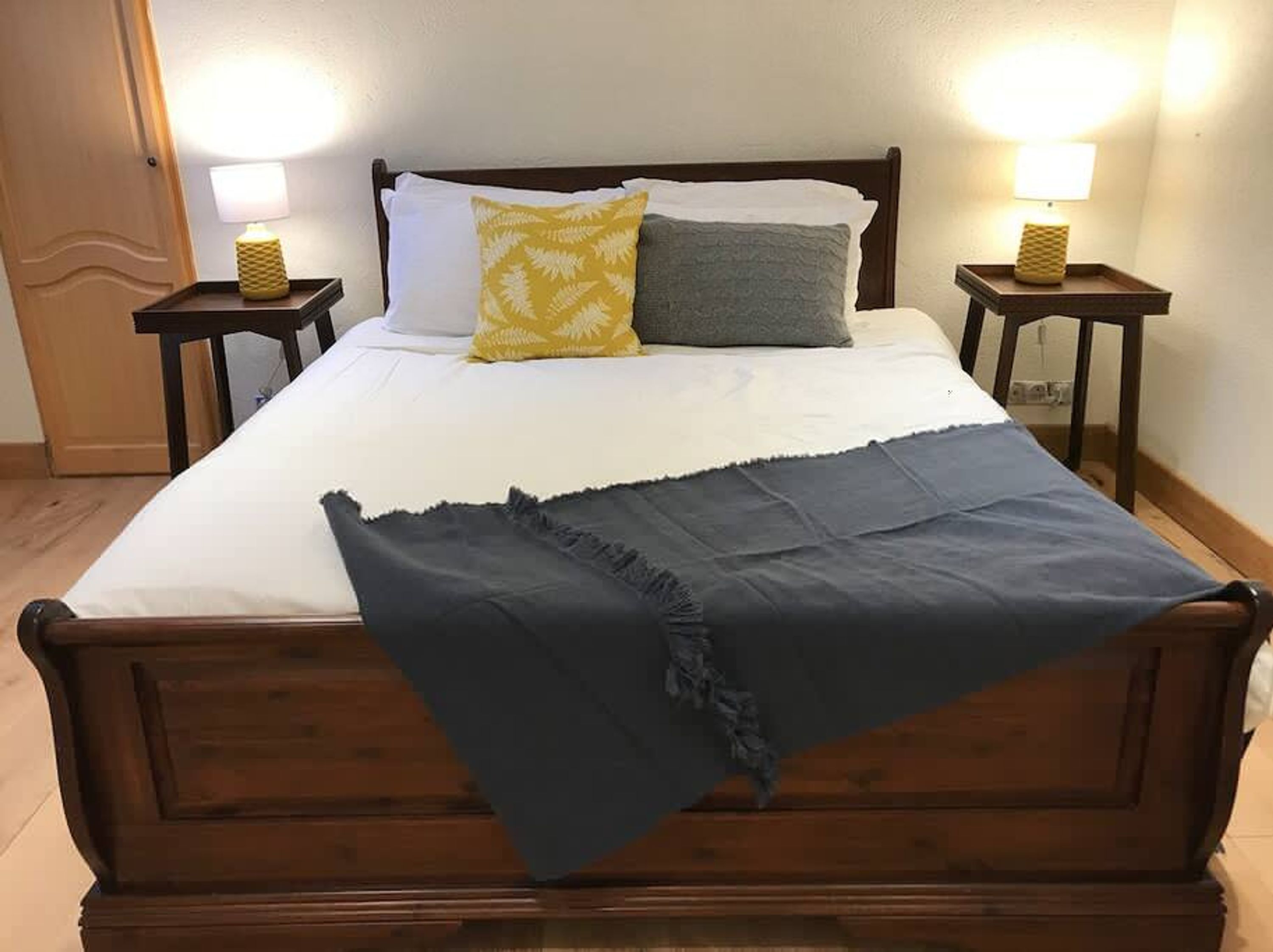 Un lit avec un cadre en bois, deux tables de chevet avec des lampes et une petite table de nuit avec une lampe.