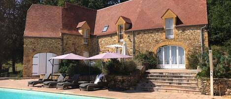 A stone building with a swimming pool, outdoor seating, and a decorative dog float.