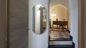 Interieur van een hal met een houten deur, een spiegel, een trap en een kamer met een lamp en een tafel.