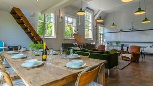 A dining area with a wooden table set for a meal, a staircase, and a green sofa. - Entire Victorian Schoolhouse With hot tub and Harbour Views (Fowey)