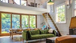 A spacious room with a dining area, a green sofa, a staircase, and large windows. - Entire Victorian Schoolhouse With hot tub and Harbour Views (Fowey)